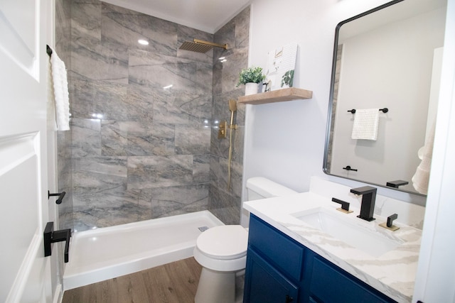 bathroom featuring wood-type flooring, vanity, a tile shower, and toilet