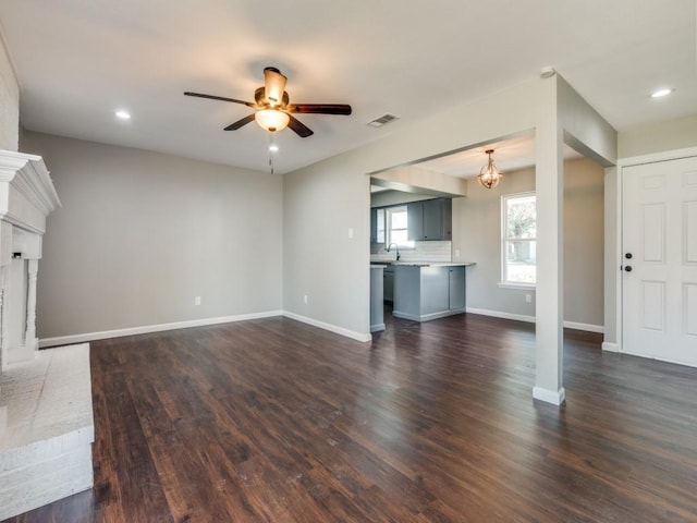 unfurnished living room with ceiling fan with notable chandelier, dark hardwood / wood-style flooring, a fireplace, and sink