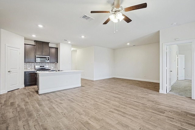 kitchen featuring backsplash, stove, a kitchen island with sink, dark brown cabinets, and light wood-type flooring