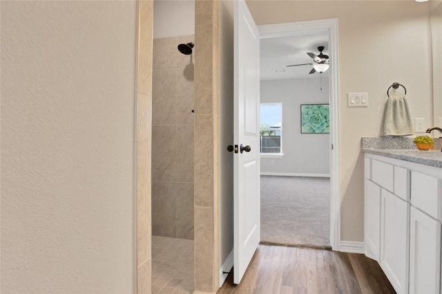 bathroom with ceiling fan, vanity, wood-type flooring, and tiled shower