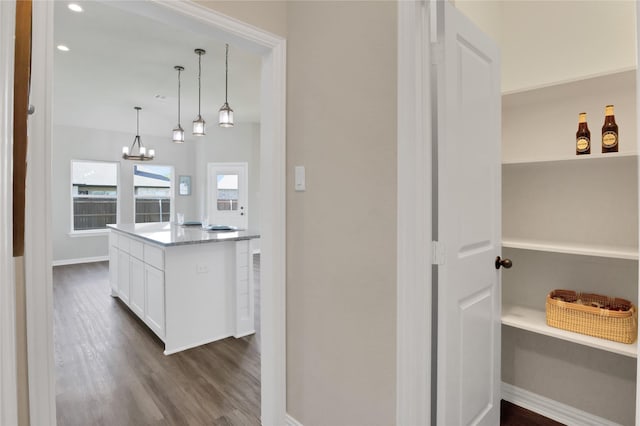 kitchen with light stone countertops, white cabinetry, dark wood-type flooring, an inviting chandelier, and decorative light fixtures