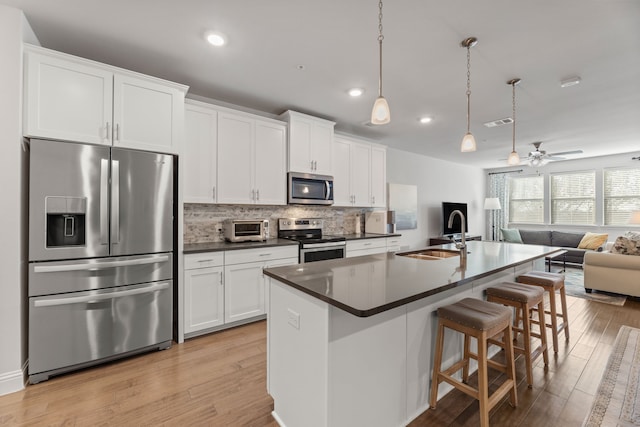 kitchen featuring white cabinets, appliances with stainless steel finishes, a center island with sink, and light hardwood / wood-style flooring