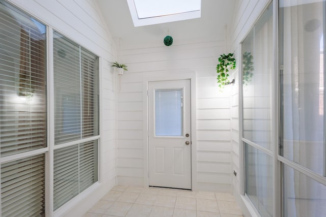 doorway with wood walls, lofted ceiling, and light tile patterned floors