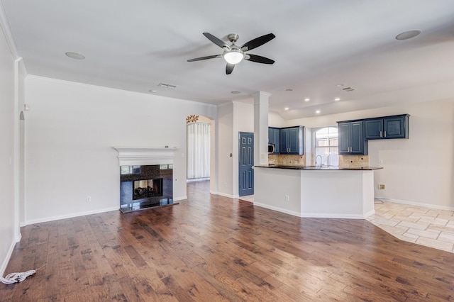 unfurnished living room featuring sink, dark wood-type flooring, a premium fireplace, and ceiling fan