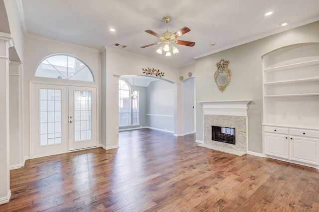 unfurnished living room featuring hardwood / wood-style flooring, built in features, ceiling fan, a high end fireplace, and ornamental molding