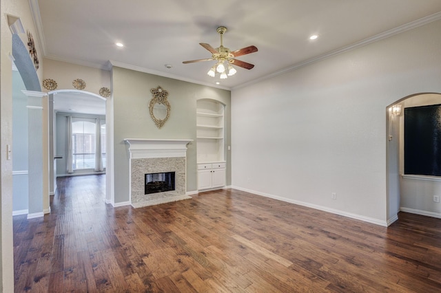 unfurnished living room with built in shelves, crown molding, dark hardwood / wood-style flooring, and ceiling fan