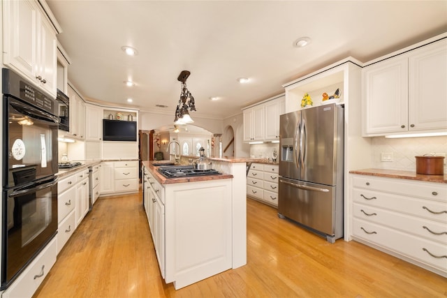 kitchen with black appliances, light hardwood / wood-style floors, white cabinetry, hanging light fixtures, and an island with sink