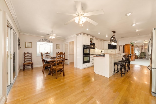 kitchen with white cabinets, light hardwood / wood-style flooring, hanging light fixtures, and a kitchen island with sink