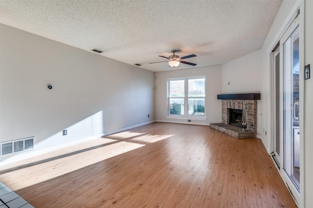 unfurnished living room featuring a fireplace, a textured ceiling, light hardwood / wood-style floors, and ceiling fan