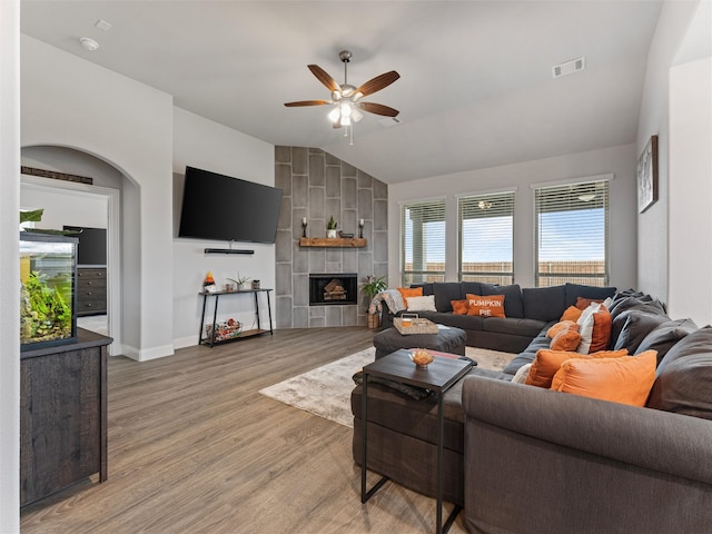 living room featuring ceiling fan, light hardwood / wood-style flooring, a tile fireplace, and vaulted ceiling