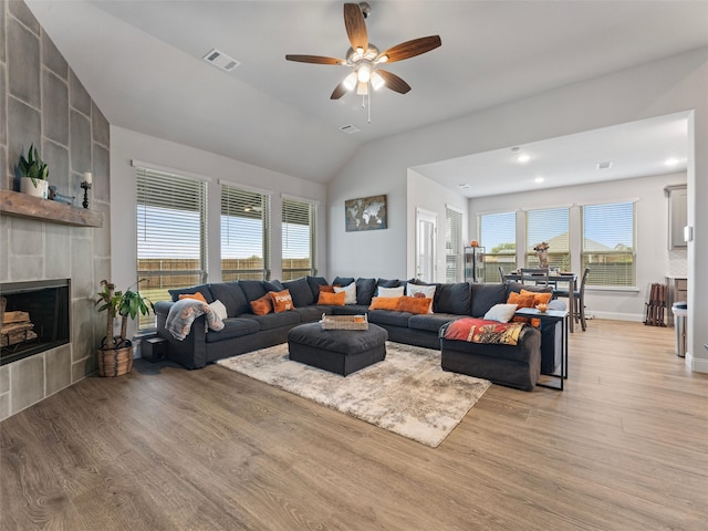 living room featuring a tile fireplace, ceiling fan, lofted ceiling, and light wood-type flooring