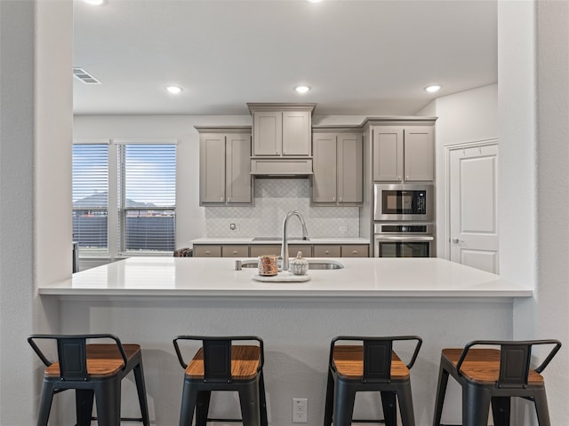 kitchen featuring kitchen peninsula, a kitchen breakfast bar, gray cabinetry, and stainless steel oven