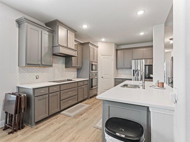 kitchen with sink, stainless steel appliances, a kitchen breakfast bar, gray cabinets, and light wood-type flooring