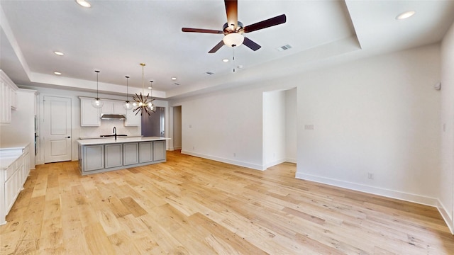 kitchen with a raised ceiling, light hardwood / wood-style flooring, an island with sink, and pendant lighting