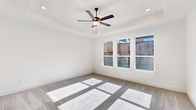 carpeted empty room featuring ceiling fan and a raised ceiling