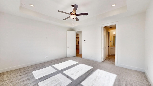 unfurnished bedroom featuring ensuite bathroom, ceiling fan, a raised ceiling, and light carpet