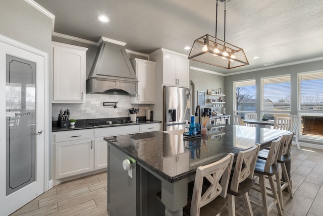 kitchen featuring a center island, stainless steel refrigerator with ice dispenser, black electric cooktop, white cabinets, and custom range hood