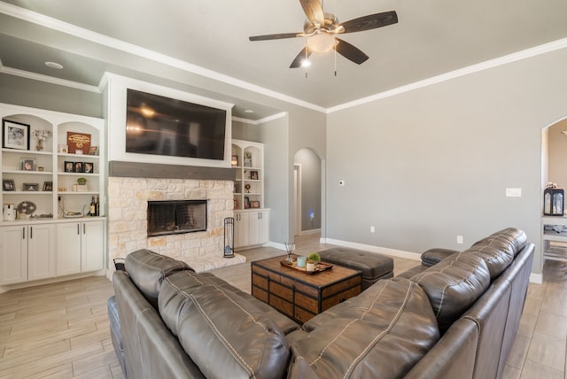 living room with built in shelves, ceiling fan, a fireplace, and ornamental molding