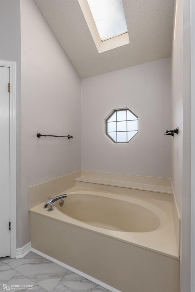 bathroom with vaulted ceiling with skylight, a textured ceiling, and a tub