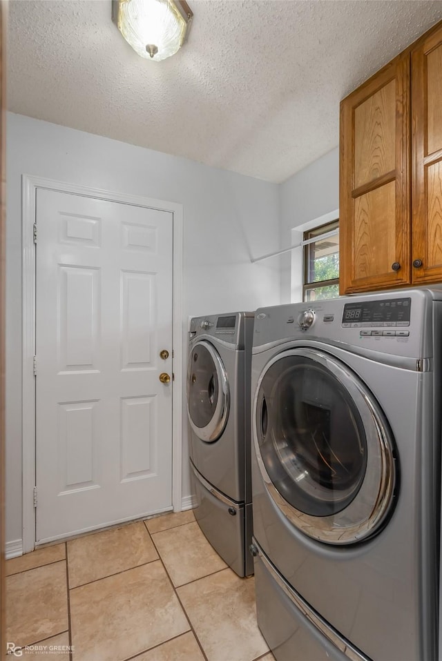 washroom featuring light tile patterned floors, washer and clothes dryer, cabinets, and a textured ceiling