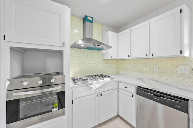 kitchen featuring tasteful backsplash, light stone counters, wall chimney exhaust hood, stainless steel appliances, and white cabinetry