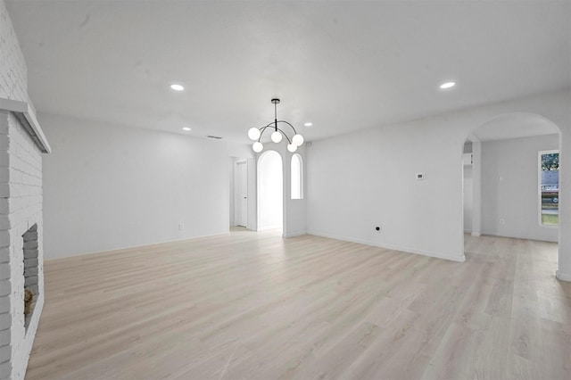 unfurnished living room with an inviting chandelier, light hardwood / wood-style flooring, and a brick fireplace