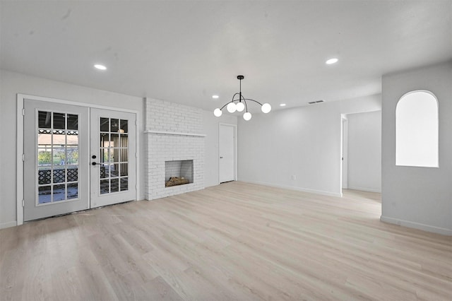 unfurnished living room with light hardwood / wood-style flooring, an inviting chandelier, french doors, and a brick fireplace