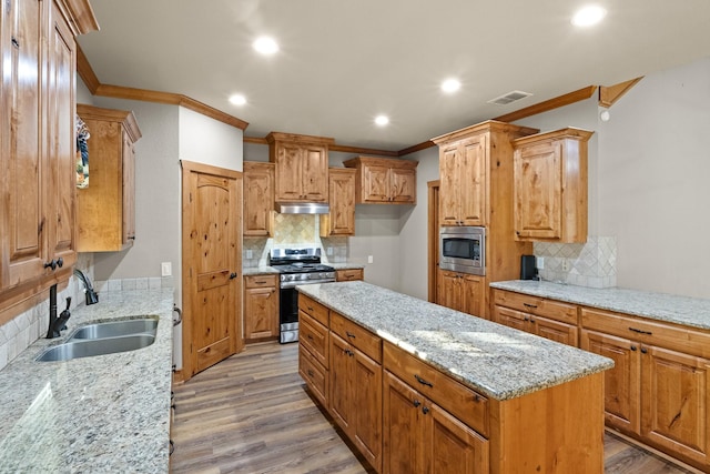 kitchen with appliances with stainless steel finishes, tasteful backsplash, sink, light stone countertops, and light hardwood / wood-style flooring