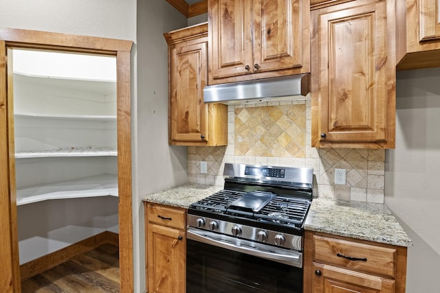 kitchen featuring stainless steel gas stove, light stone counters, dark hardwood / wood-style floors, and decorative backsplash