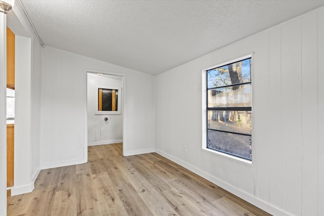 unfurnished room with vaulted ceiling, a textured ceiling, and light wood-type flooring