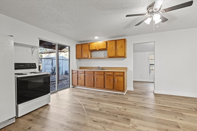 kitchen with light wood-type flooring, a textured ceiling, white appliances, and sink