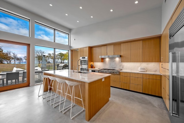 kitchen with a kitchen bar, a towering ceiling, stainless steel appliances, a kitchen island with sink, and decorative backsplash