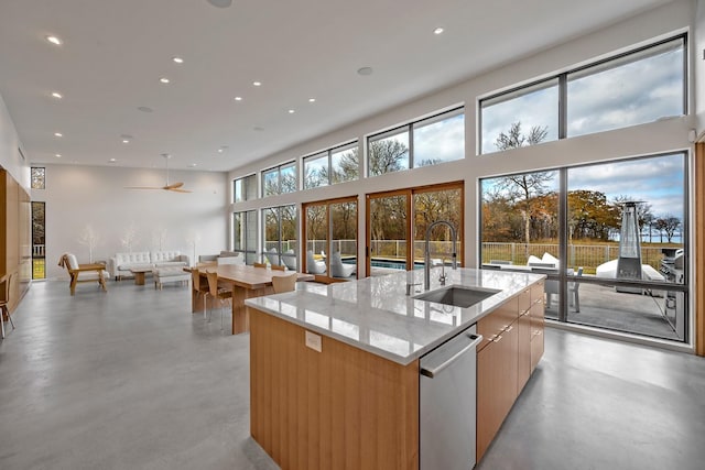 kitchen featuring light stone counters, stainless steel dishwasher, sink, and an island with sink