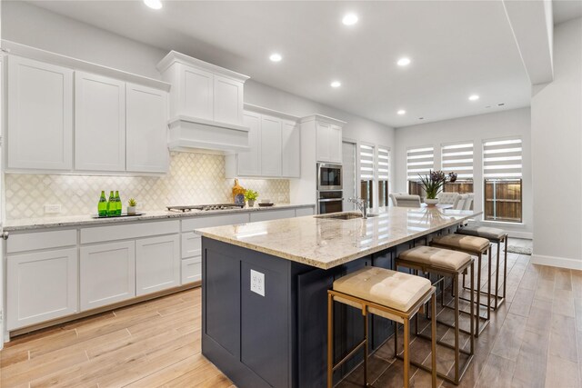 kitchen with white cabinets, a breakfast bar, an island with sink, and light hardwood / wood-style floors