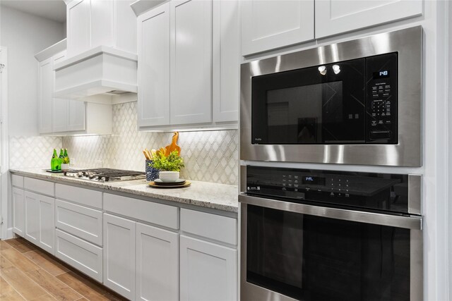 kitchen with white cabinets, light wood-type flooring, light stone counters, and built in microwave