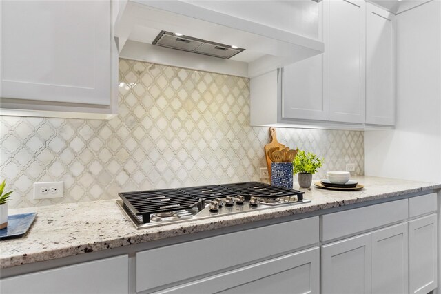 kitchen featuring stainless steel gas stovetop, wall chimney exhaust hood, white cabinets, and light stone countertops