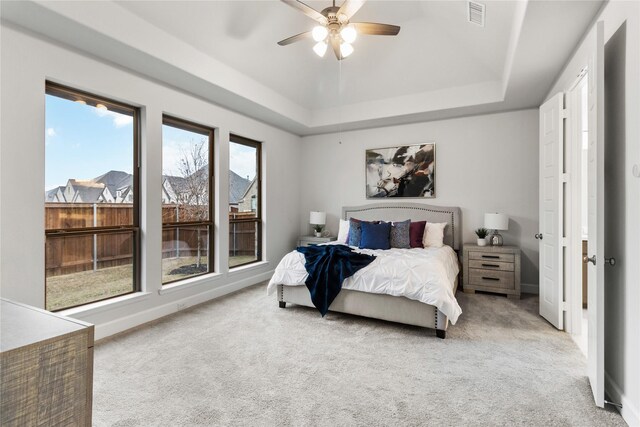 carpeted bedroom with ceiling fan and a tray ceiling