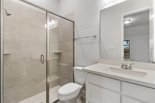 bathroom featuring a shower with door, vanity, and toilet