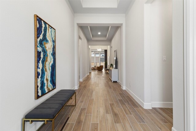 hallway featuring a raised ceiling, light wood-type flooring, and a chandelier