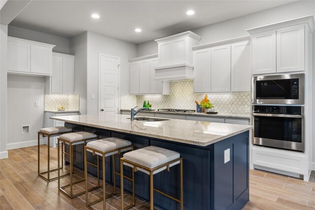 kitchen with a center island with sink, light wood-type flooring, sink, and appliances with stainless steel finishes