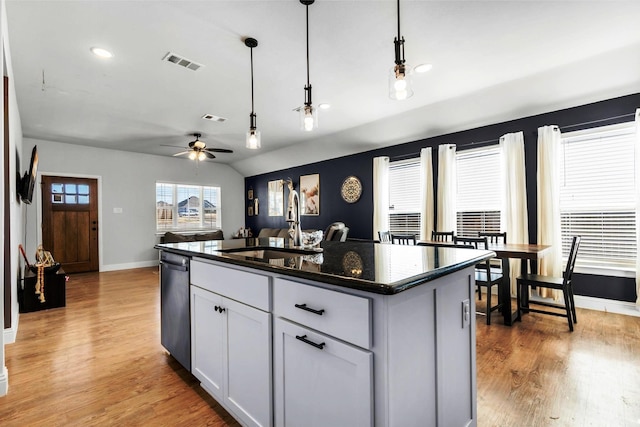 kitchen with an island with sink, stainless steel dishwasher, decorative light fixtures, and light wood-type flooring