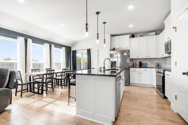 kitchen featuring appliances with stainless steel finishes, pendant lighting, a center island with sink, light hardwood / wood-style floors, and lofted ceiling