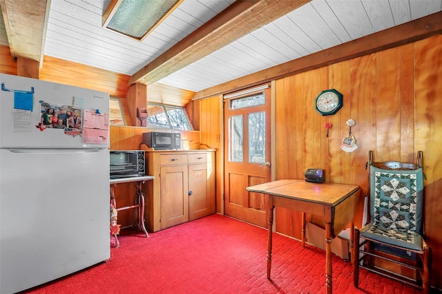 kitchen featuring white refrigerator, beam ceiling, carpet floors, and wood walls