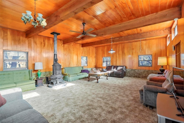 carpeted living room featuring wood ceiling, wooden walls, ceiling fan with notable chandelier, beamed ceiling, and a wood stove