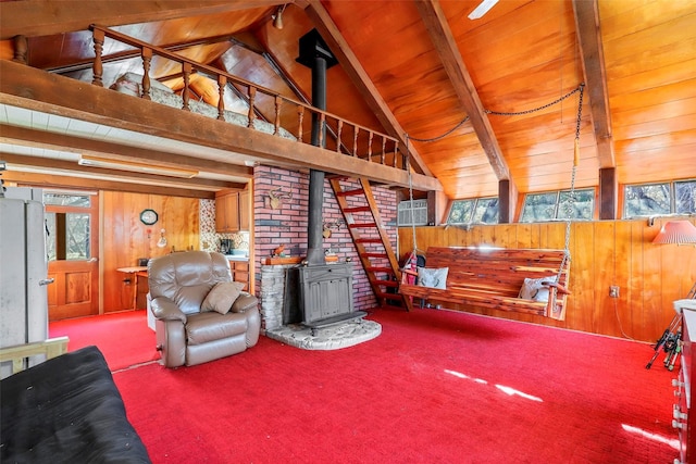 living room with vaulted ceiling with beams, wood ceiling, a wood stove, wooden walls, and carpet floors