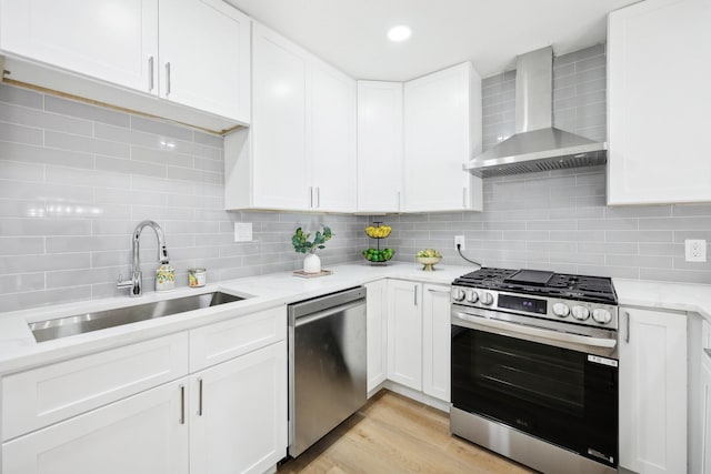 kitchen with appliances with stainless steel finishes, backsplash, sink, wall chimney range hood, and white cabinetry