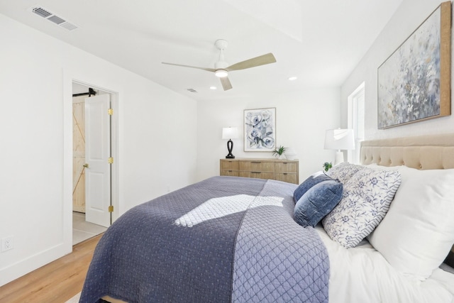 bedroom with a barn door, hardwood / wood-style flooring, and ceiling fan