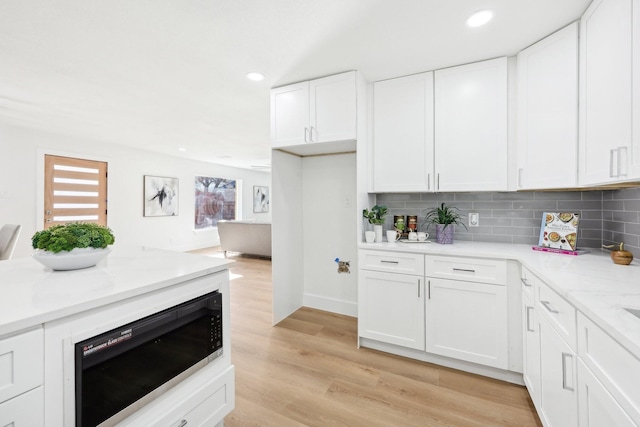 kitchen featuring white cabinets, tasteful backsplash, light hardwood / wood-style floors, light stone counters, and black microwave