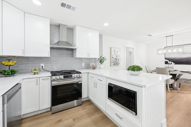 kitchen featuring white cabinets, wall chimney exhaust hood, kitchen peninsula, and stainless steel appliances