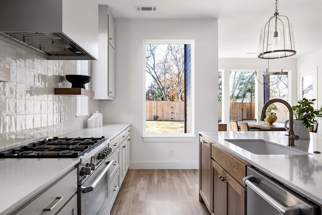 kitchen with stainless steel appliances, light hardwood / wood-style flooring, a wealth of natural light, and wall chimney exhaust hood